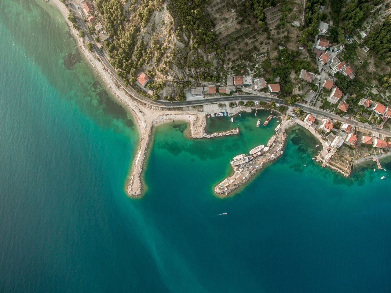 Flygfoto av en kustby med turkost vatten och båtar nära stranden.