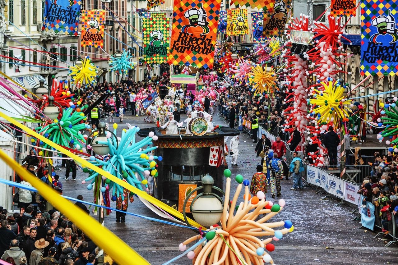 Karneval in Rijeka, mit bunten Luftballon-Dekorationen und Festwagen, die durch eine belebte Straße ziehen. Menschenmengen säumen die Straßen und feiern das Fest.