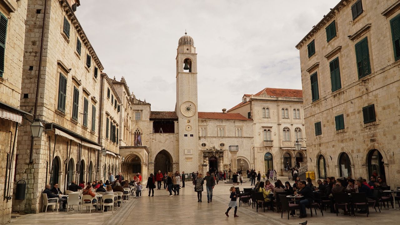 Plads foran klokketårnet og Sponza-paladset i Dubrovnik, med mennesker i caféer