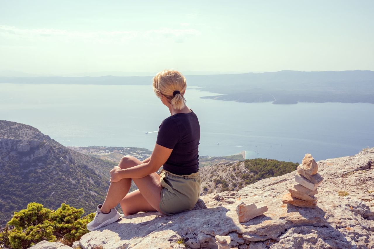 Eine Frau sitzt auf einem Felsen am Gipfel des Vidova Gora auf der Insel Brač und genießt die Aussicht auf das Meer und die umliegenden Inseln.