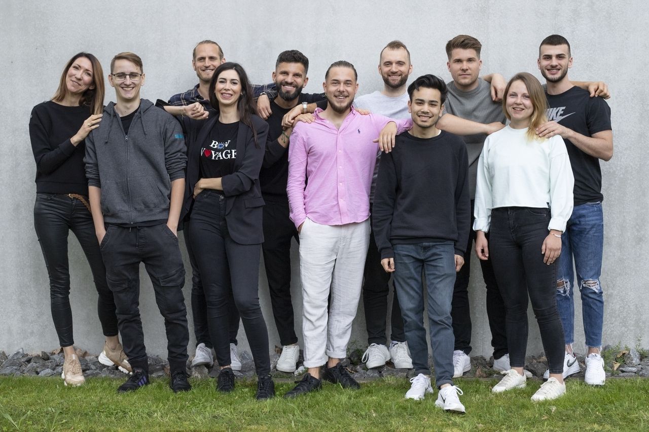 Het Crovillas team lacht en poseert voor een groepsfoto voor een grijze muur.