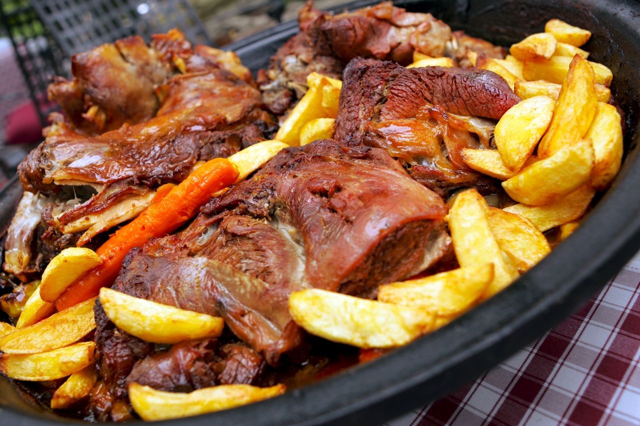 Traditionel kroatisk peka med braiseret kød, kartofler og gulerødder i en støbejernspande på et konoba-bord.
