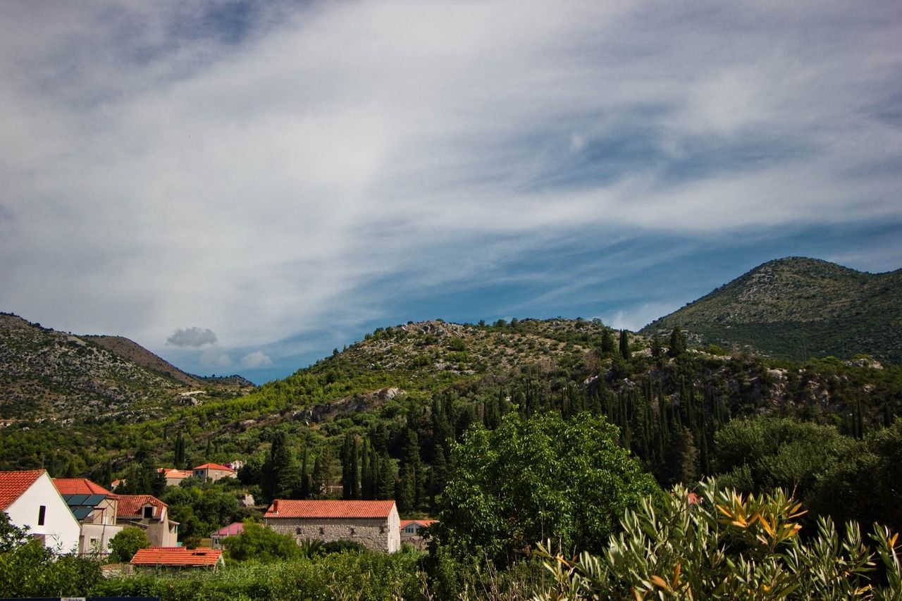 Malersiches Dorf in Kroatien, eingebettet in eine hügelige Landschaft mit üppiger Vegetation und traditionellen Häusern mit roten Dächern. Der klare Himmel und die grünen Hügel schaffen eine friedliche und idyllische Atmosphäre.