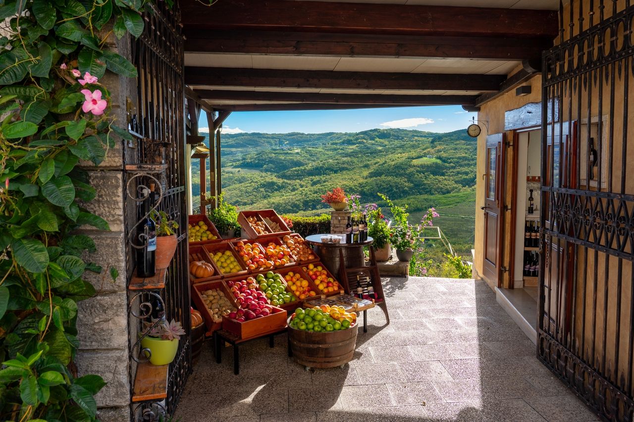 Un mercato rustico a Motovun che offre frutta e verdura fresca e una vista pittoresca sulle colline e valli verdi sullo sfondo. Il mercato è decorato con casse di legno, barili e bottiglie di vino.