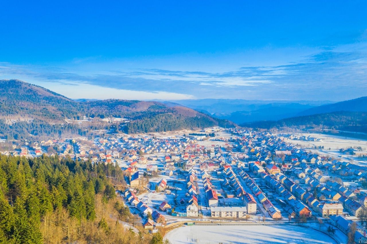 Vinterlig udsigt over en lille by i Kroatien, indlejret i et bakket landskab og omgivet af snedækkede skove. Den klare, kolde luft og den blå himmel giver scenen en rolig og idyllisk atmosfære.