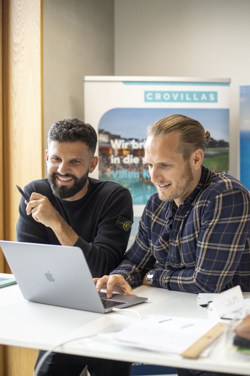 Valentino ja Dogan istuvat pöydän ääressä ja työskentelevät kannettavalla tietokoneella.