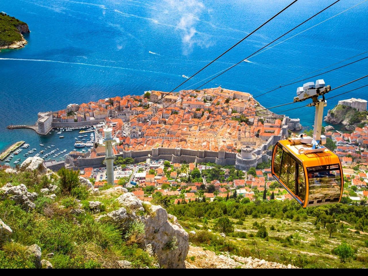 Hırvatistan'daki Dubrovnik'in tarihi şehir merkezine teleferikten nefes kesici bir bakış. Kırmızı çatıları, büyük şehir surları ve Adriyatik'in berrak, mavi suları bu tarihi şehri popüler bir turistik yer yapar.