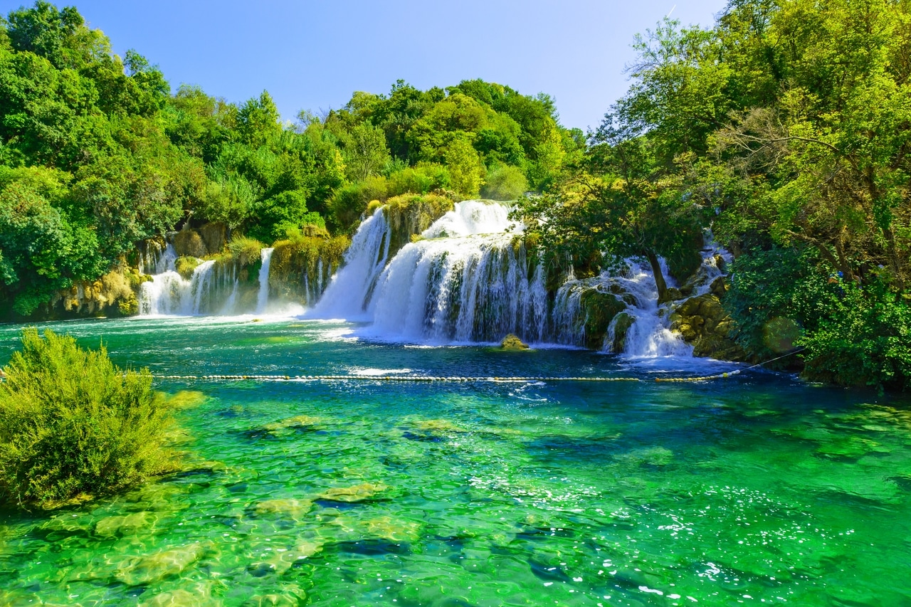 Praktfulla vattenfall i nationalparken Krka i Kroatien, omgivna av frodig, grön vegetation. Det klara, smaragdgröna vattnet och parkens naturliga skönhet erbjuder en idyllisk och uppfriskande naturupplevelse.