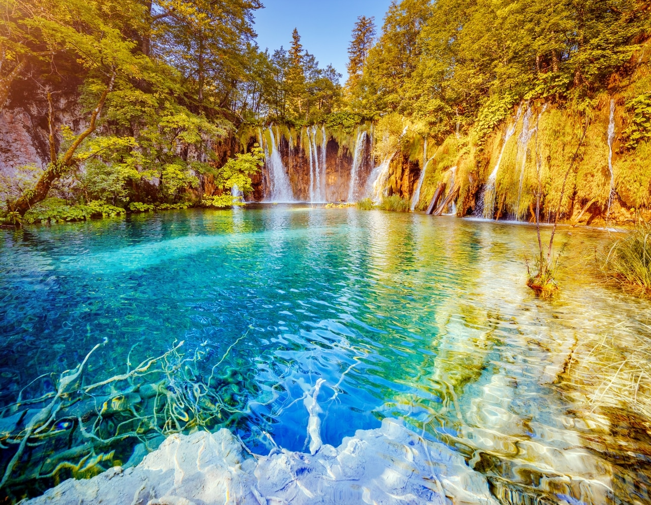 Malersiche Wasserfälle und kristallklares Wasser im Plitvicer Seen Nationalpark in Kroatien, umgeben von üppiger Vegetation. Die natürliche Schönheit und das smaragdgrüne Wasser machen diesen Ort zu einem beliebten Reiseziel.