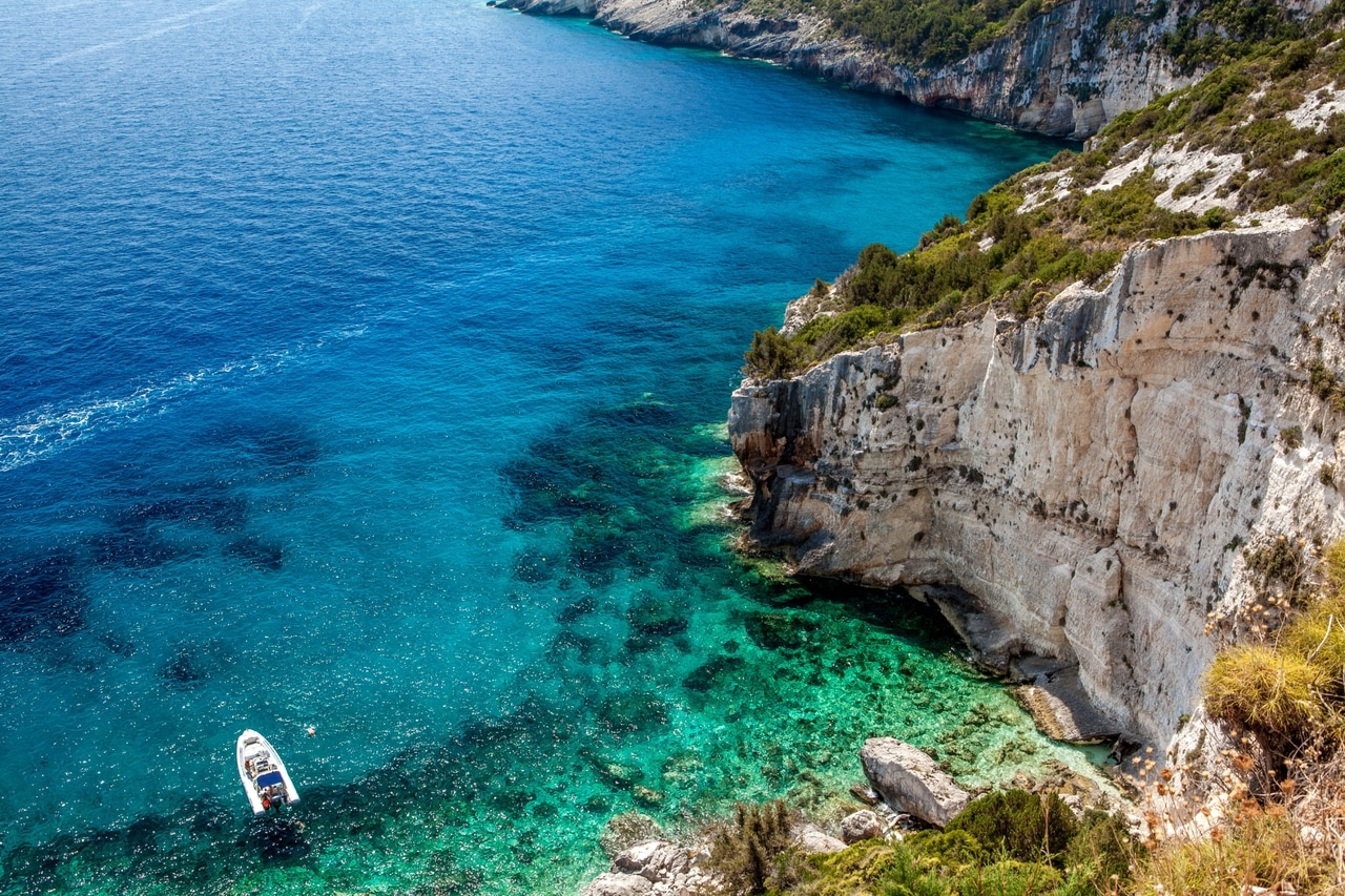 Atemberaubende Aussicht auf eine felsige Küste in Kroatien mit kristallklarem, türkisfarbenem Wasser. Ein kleines Boot ankert in der Bucht, umgeben von üppiger Vegetation und steilen Klippen, die die natürliche Schönheit der Adria hervorheben.