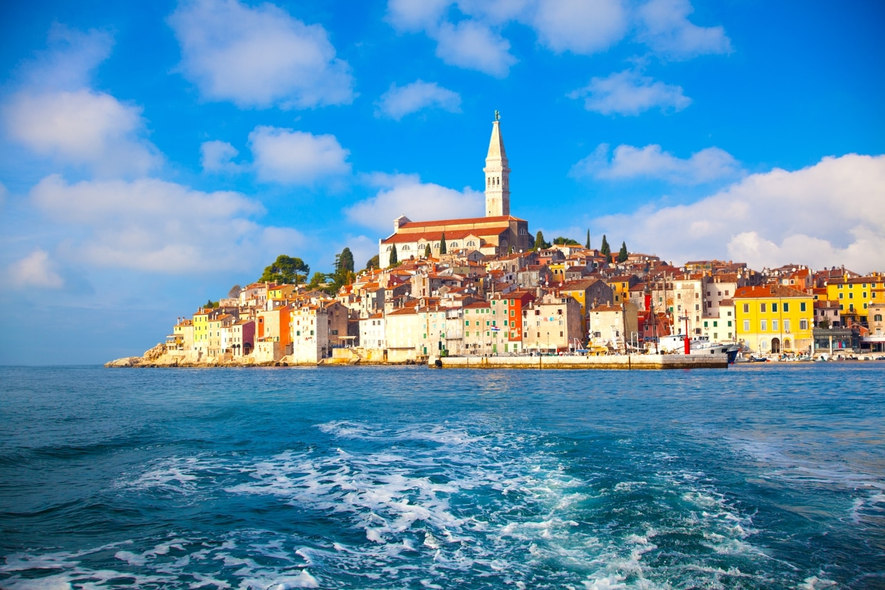 Panoramski pogled na obalni grad Rovinj u Istri, Hrvatska, s njegovim šarenim zgradama i prepoznatljivom crkvom svete Eufemije. Grad se slikovito nalazi na obali Jadrana pod vedrim plavim nebom.