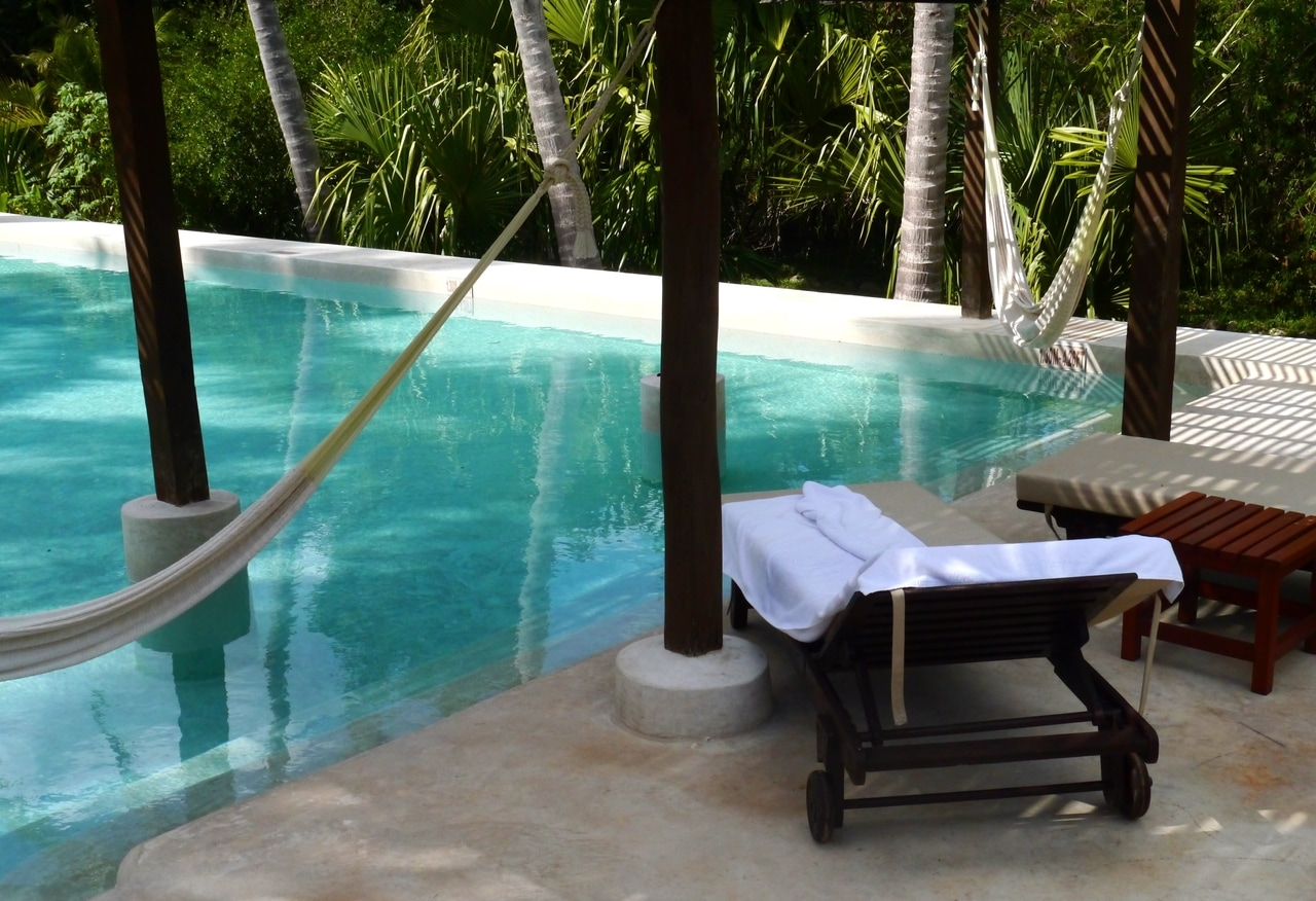 Espace détente au bord de la piscine avec un hamac et une chaise longue dans un complexe tropical. L'atmosphère paisible et l'eau claire et bleue offrent l'endroit parfait pour se détendre et se ressourcer.