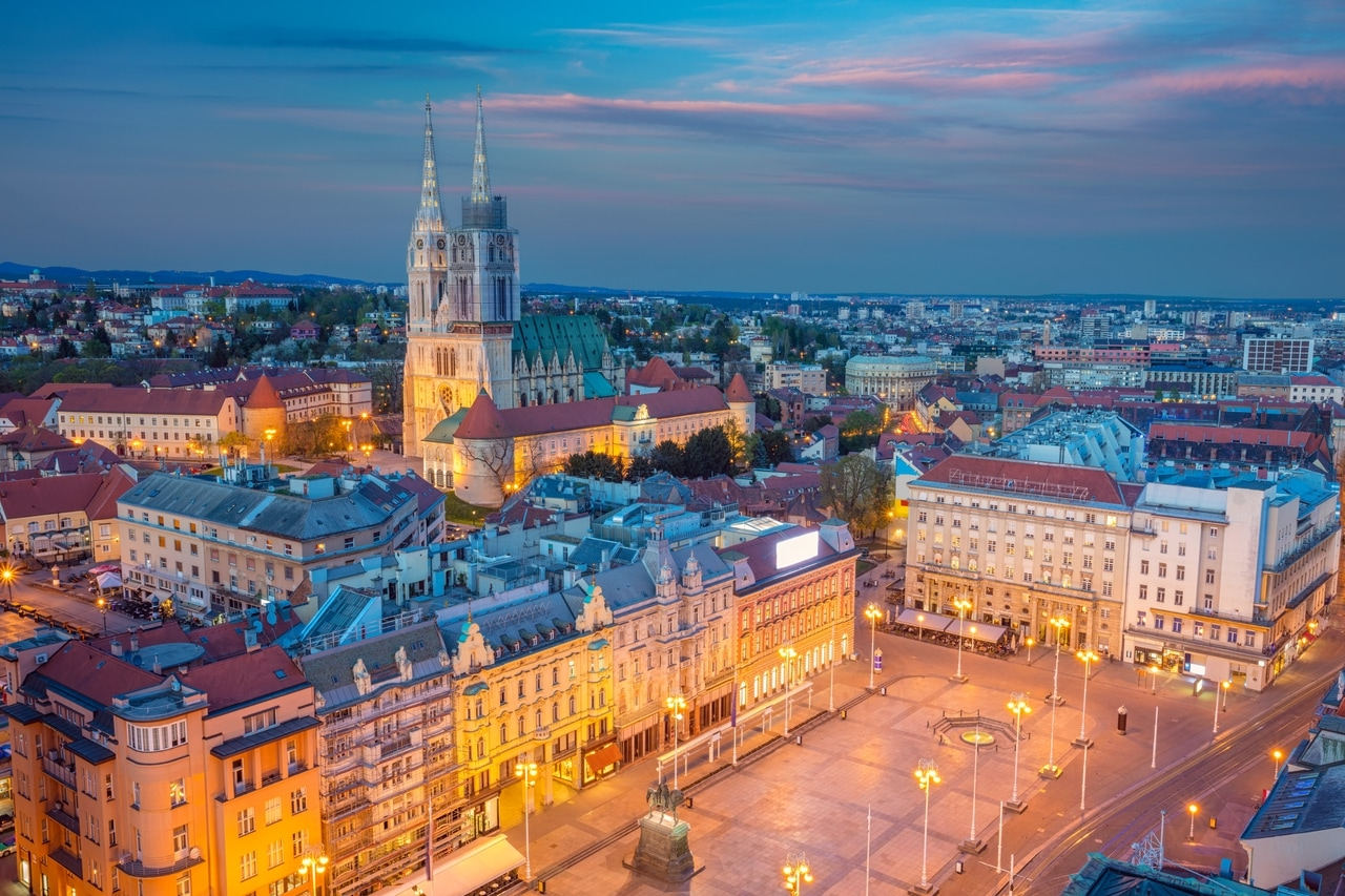 Aftenudsigt over Ban-Jelačić-pladsen og katedralen i Zagreb i Kroatien. De oplyste bygninger og historiske vartegn afspejler byens kulturelle og arkitektoniske mangfoldighed.