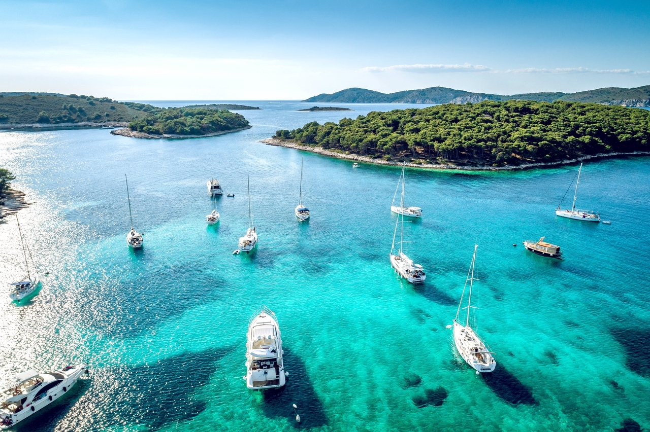 Segelbåtar och yachter i en pittoresk vik vid Hvar, Kroatien, med turkost vatten och skogsklädda öar i bakgrunden